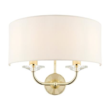 Gallery Direct Ostwyn 2 light wall fitting with vintage white half-drum fabric shade, brass curved arms and clear crystal accents on a round backplate.