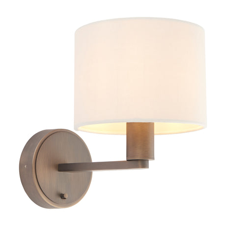 Gallery Direct Delyra wall light with cream faux silk drum shade, antique bronze round backplate, slim arm, and on/off switch on a white background.