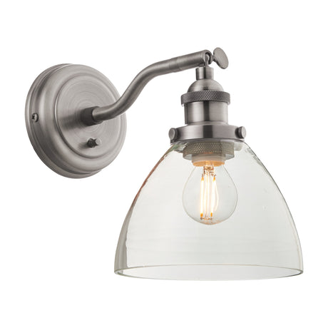 Gallery Direct Sarwen industrial wall light with brushed silver steel arm, knurled detailing and clear glass dome shade around an E27 filament bulb.