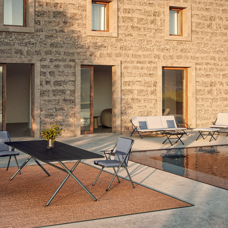 Garda Aluminium Garden Dining Chair in folding design with blue sling seat and back, set on a poolside patio beside a black outdoor dining table.