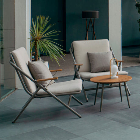 Garda high back garden armchairs in anthracite aluminium with beige sling seats, crossed X-frame sides and wood armrests, shown beside a round wood-top side table on an outdoor patio.