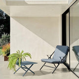 Garda square aluminium outdoor coffee table in graphite with X-shaped crossed legs, shown on a patio beside a matching lounge chair with blue cushions.