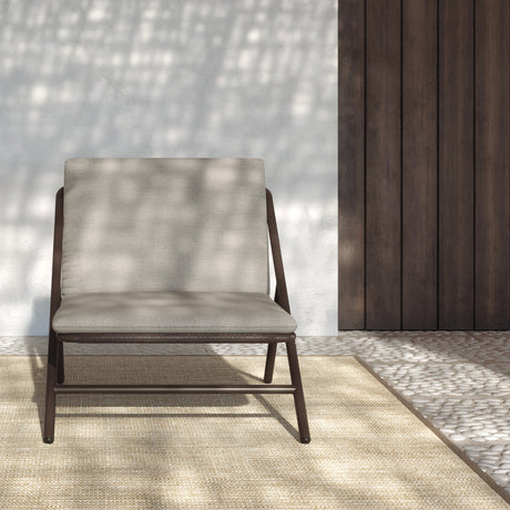 Garda High Back Garden Armchair Cushion Set in beige fabric shown fitted to a dark brown aluminium frame chair, set against a stone wall and wood panel backdrop.