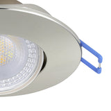 Close-up of a Gedrez round LED downlight in satin nickel, showing the tiltable integrated LED head with clear plastic lens and blue spring clip fittings, against a white background.