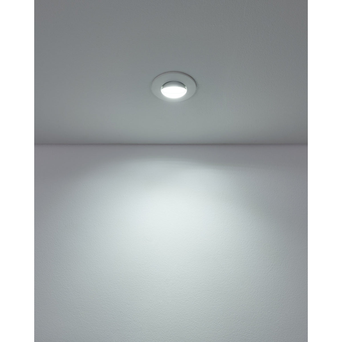 Gedrez round LED downlight in white recessed into a grey ceiling, casting a soft cool-white light beam onto the wall below.