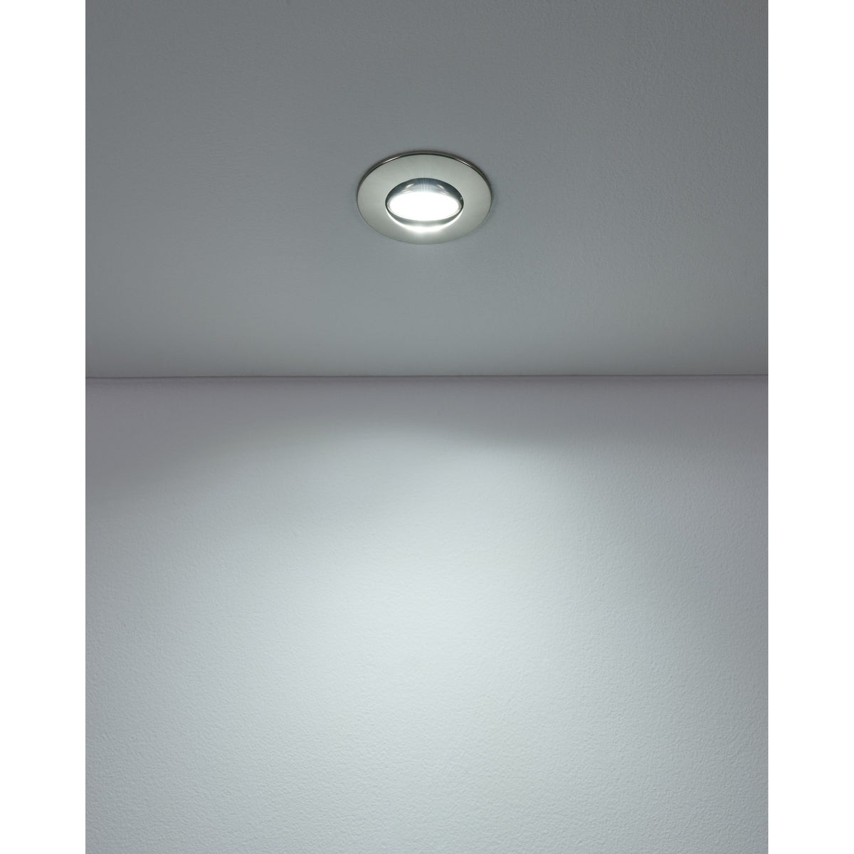 Gedrez round LED downlight in satin nickel finish, recessed in a white ceiling and shown illuminated, casting light onto the wall below.