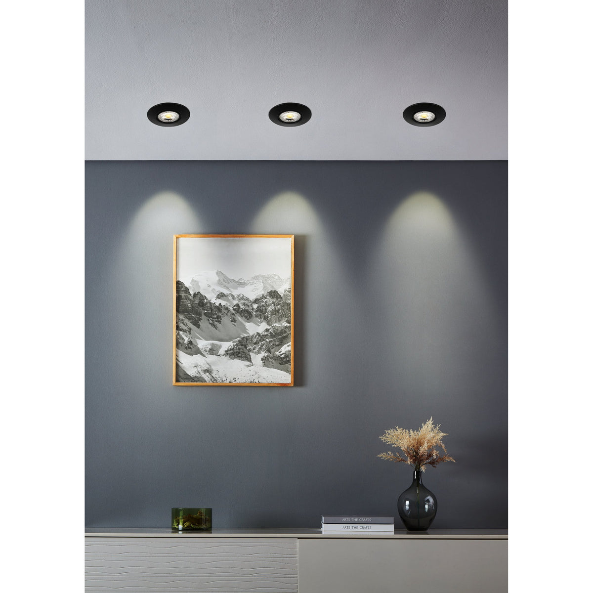 Gedrez LED Downlight Set of 7 in black, round recessed ceiling fittings shown installed above a grey wall, casting warm light over a framed mountain print and sideboard display.