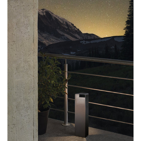 Gelbora LED outdoor post light in anthracite, rectangular aluminium column with louvred head, shown on a patio beside railings and a potted plant at dusk.
