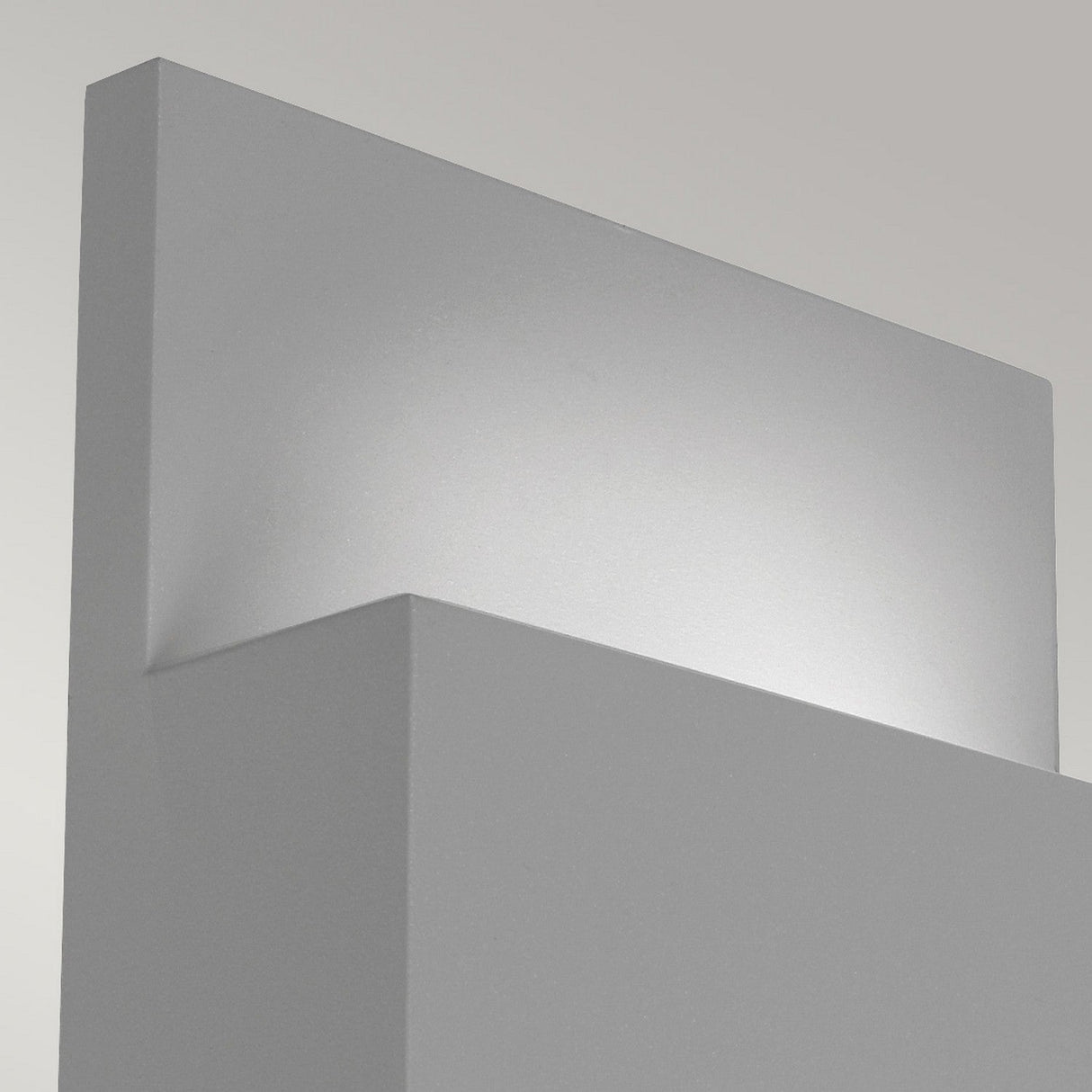 Close-up of the Geneve Outdoor 1 Light Wall Lantern in silver, a minimalist modern sconce crafted from die-cast aluminum emitting soft, indirect light. The design features clean lines and a rectangular shape, with a neutral gray tone that blends seamlessly into the background.