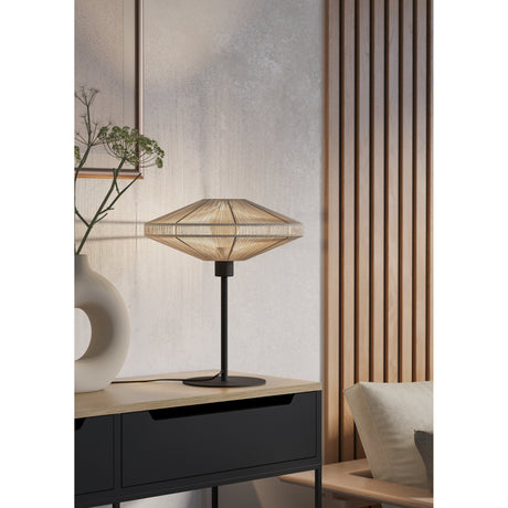 Ginvenne Table Lamp in black and cream, with a slim black steel stem, round base, and wide disc-shaped cream fabric cord shade, shown on a sideboard in a living room setting.