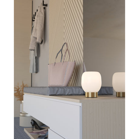 Girbena Table Lamp with rounded opal glass shade and brushed brass base, shown on a console table beside a mirror in a hallway setting.
