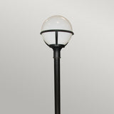 The Glenbeigh 1 Light Pillar Lantern in black, featuring a round, white globe-shaped light fixture, stands against a plain, light gray background, showcasing elegant outdoor lighting. With its IP44 rating and corrosion-proof design, this lantern ensures both style and durability in any setting.