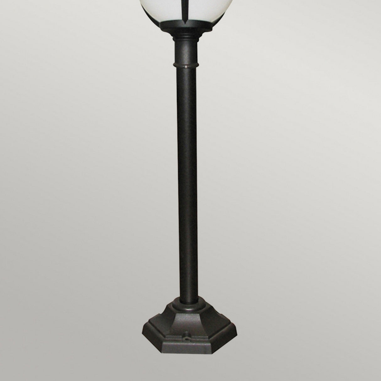 The Glenbeigh 1 Light Pillar Lantern - Black showcases a hexagonal base with a round white lamp on top, boasting an IP44 rating for dependable outdoor lighting, all set against a plain light gray background.