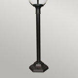 The Glenbeigh 1 Light Pillar Lantern - Black showcases a hexagonal base with a round white lamp on top, boasting an IP44 rating for dependable outdoor lighting, all set against a plain light gray background.