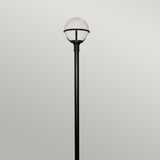 Standing against a plain gray background, the Glenbeigh 1 Light Lamp Post in black features a tall, corrosion-resistant design with a round white globe at the top for outdoor lighting.