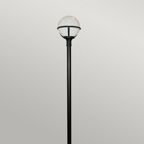 Standing against a plain gray background, the Glenbeigh 1 Light Lamp Post in black features a tall, corrosion-resistant design with a round white globe at the top for outdoor lighting.