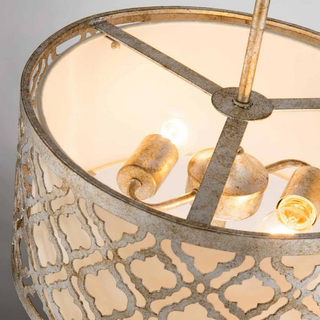 A close-up of the Arabella 2 Light Duo-Mount Medium Pendant/Semi-Flush showcases its rustic charm with a geometric gold metal design and three exposed LED lamps casting a warm glow. The metal's weathered, antique finish enhances the fixture's vintage appeal.