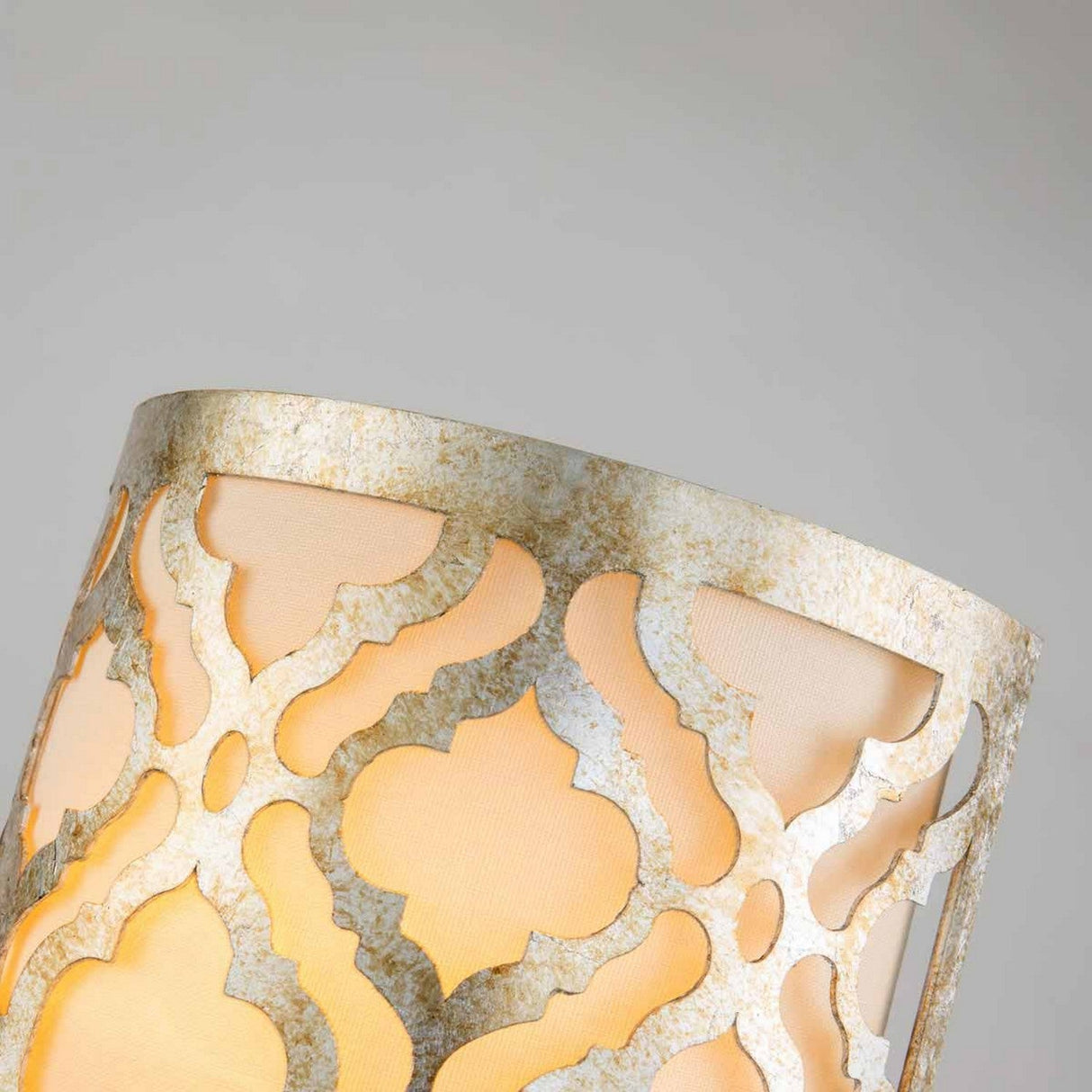 Here is a rewritten version using the product data:

A close-up of the Arabella 1 Light Wall Light showcases its ornate ivory shade adorned with an intricate geometric cutout pattern. The warm glow gently diffuses through, casting soft shadows, while its textured gold metal finish enhances elegance and artistry, creating a captivating ambiance.