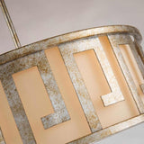 Close-up of a decorative round lampshade showcasing a geometric Grecian key motif with metallic, weathered details. The neutral beige background emits a warm glow, highlighting the vintage elegance of the Lemuria 3 Light Duo-Mount Large Pendant/Semi-Flush in Gold with an Ivory Shade design.