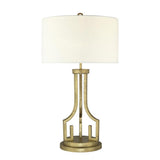 The Lemuria 1 Light Table Lamp - Gold With Ivory Shade showcases a decorative concept, featuring a large ivory cylindrical lampshade and an artistic geometric metallic base in a lavish gold finish.