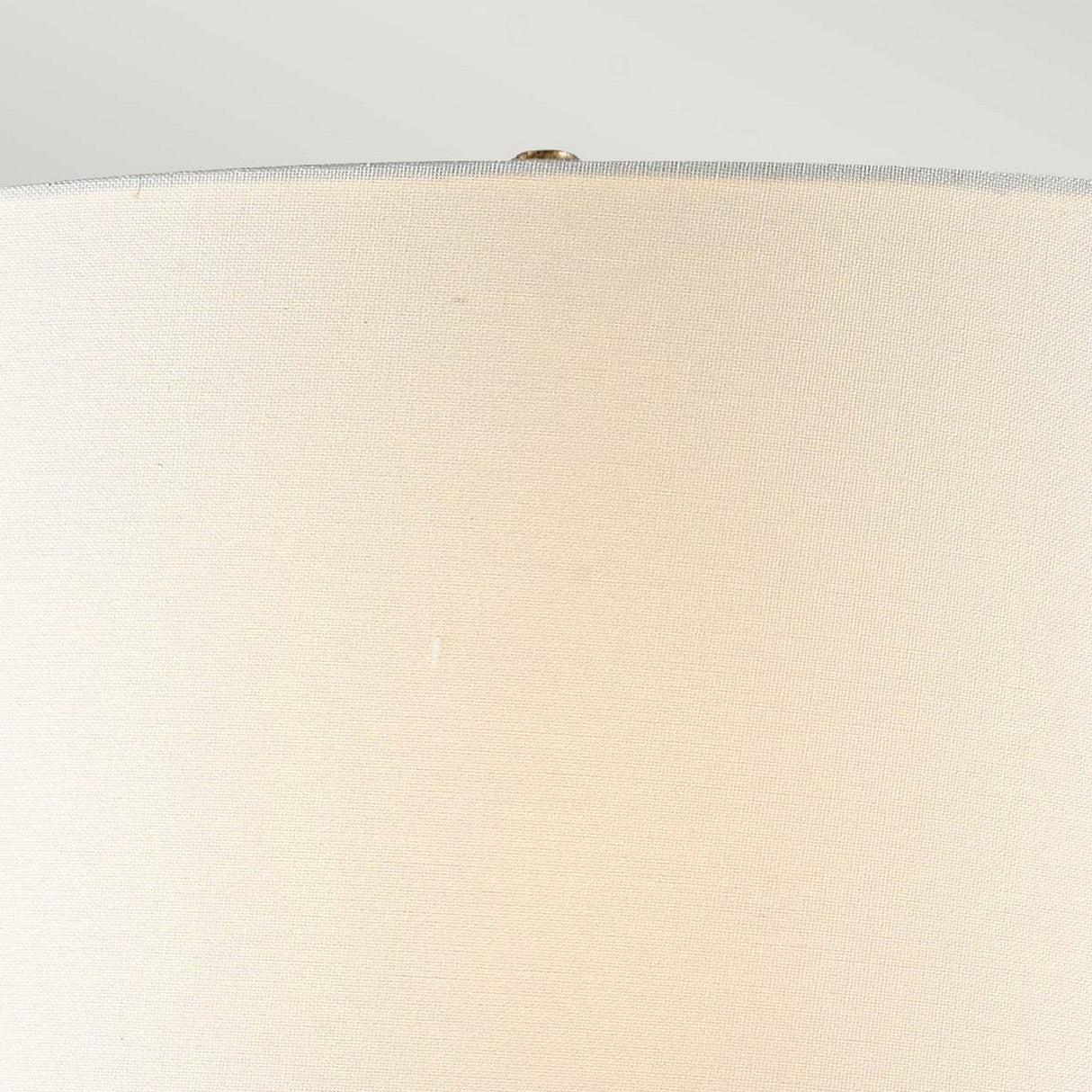 Close-up view of the Octavia 1 Light Table Lamp's ivory shade against a light background. The texture of the fabric is visible, highlighted by a small metallic finial at the top.