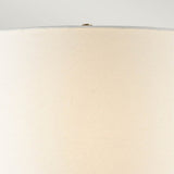 Close-up view of the Octavia 1 Light Table Lamp's ivory shade against a light background. The texture of the fabric is visible, highlighted by a small metallic finial at the top.