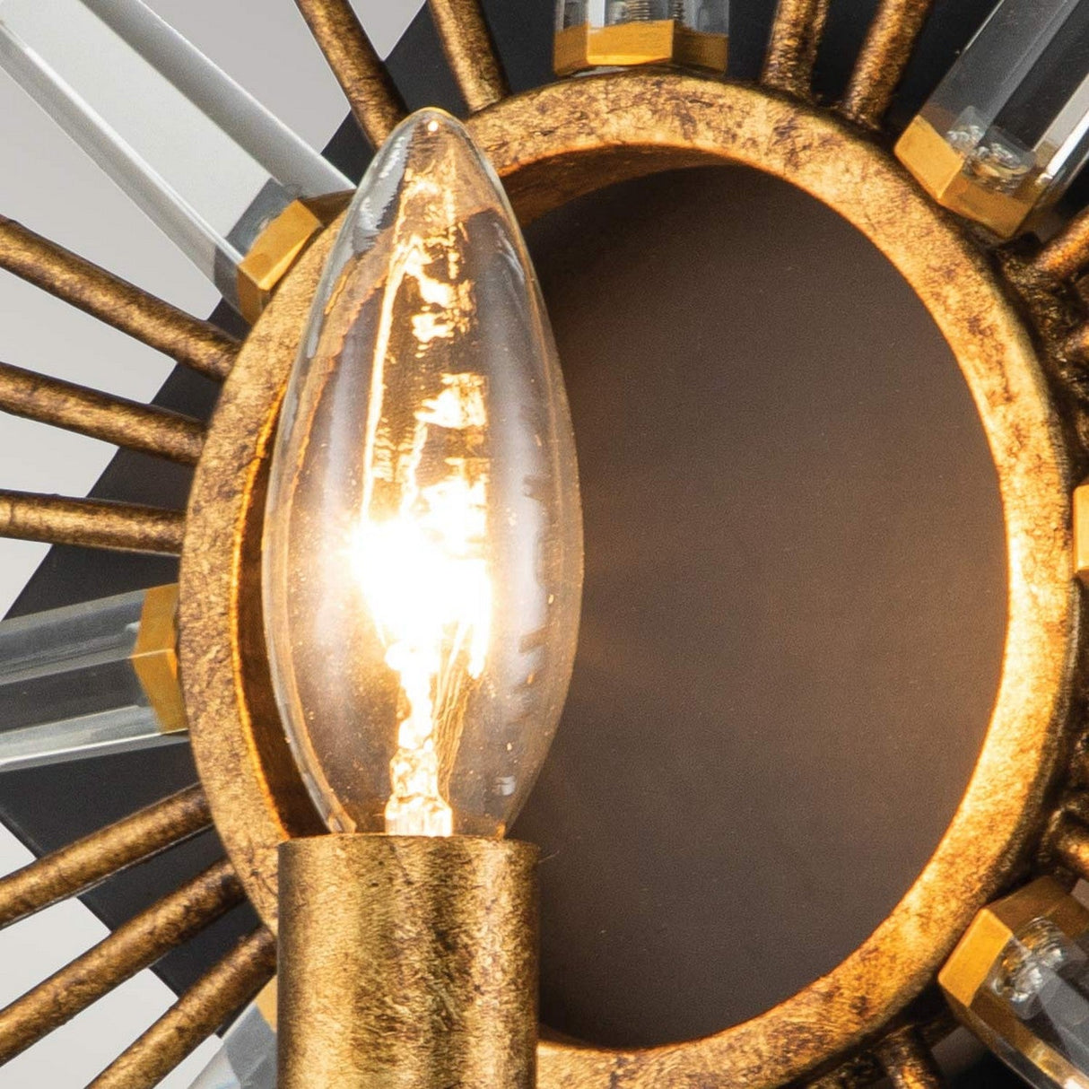 Close-up of the Sun King 1 Light Wall in Gold Leaf, showcasing a lit bulb in an ornate fixture against a circular black background. The design features gold leaf and transparent rod-like elements that form a sunburst pattern, enhanced with K9 cut glass crystals for added brilliance.