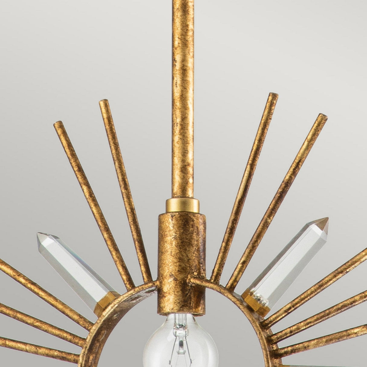 Close-up of the Sun King 1 Light Pendant in Gold Leaf, showcasing a central light bulb encased by a decorative circular frame in a starburst design. Radiating metal rods and crystal prisms extend outward, forming an adjustable pendant light against a soft grey background.