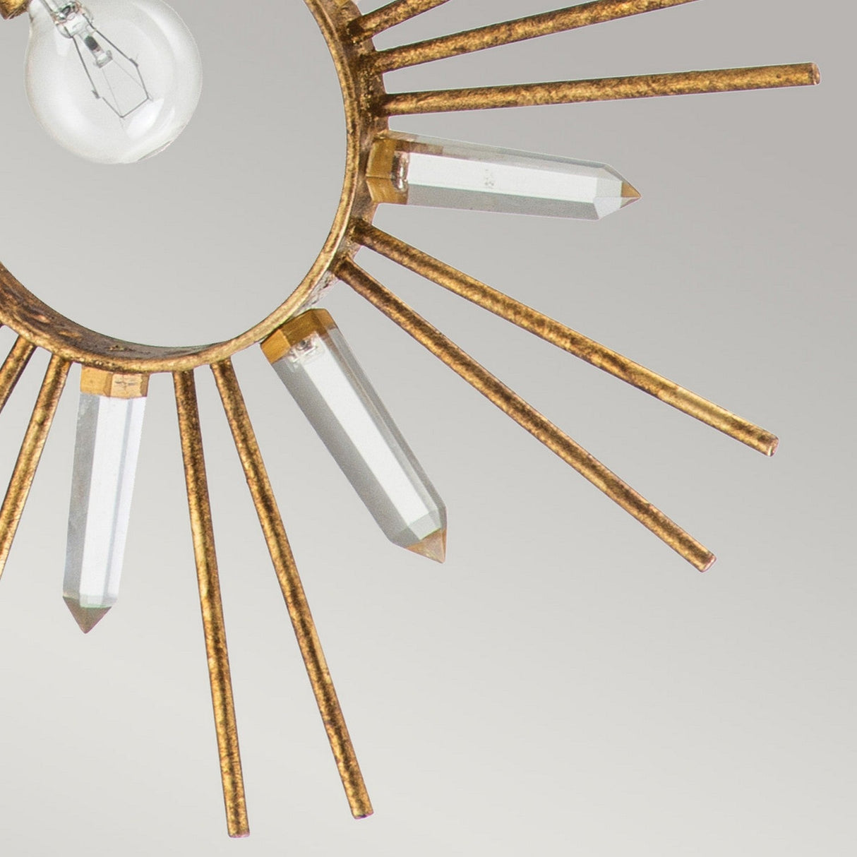A close-up of the Sun King 1 Light Pendant - Gold Leaf reveals its adjustable pendant light with a starburst design, showcasing a golden sunburst and gold leaf finish. The clear crystal rods extend from the circular frame, encircling a visible light bulb against a neutral background.