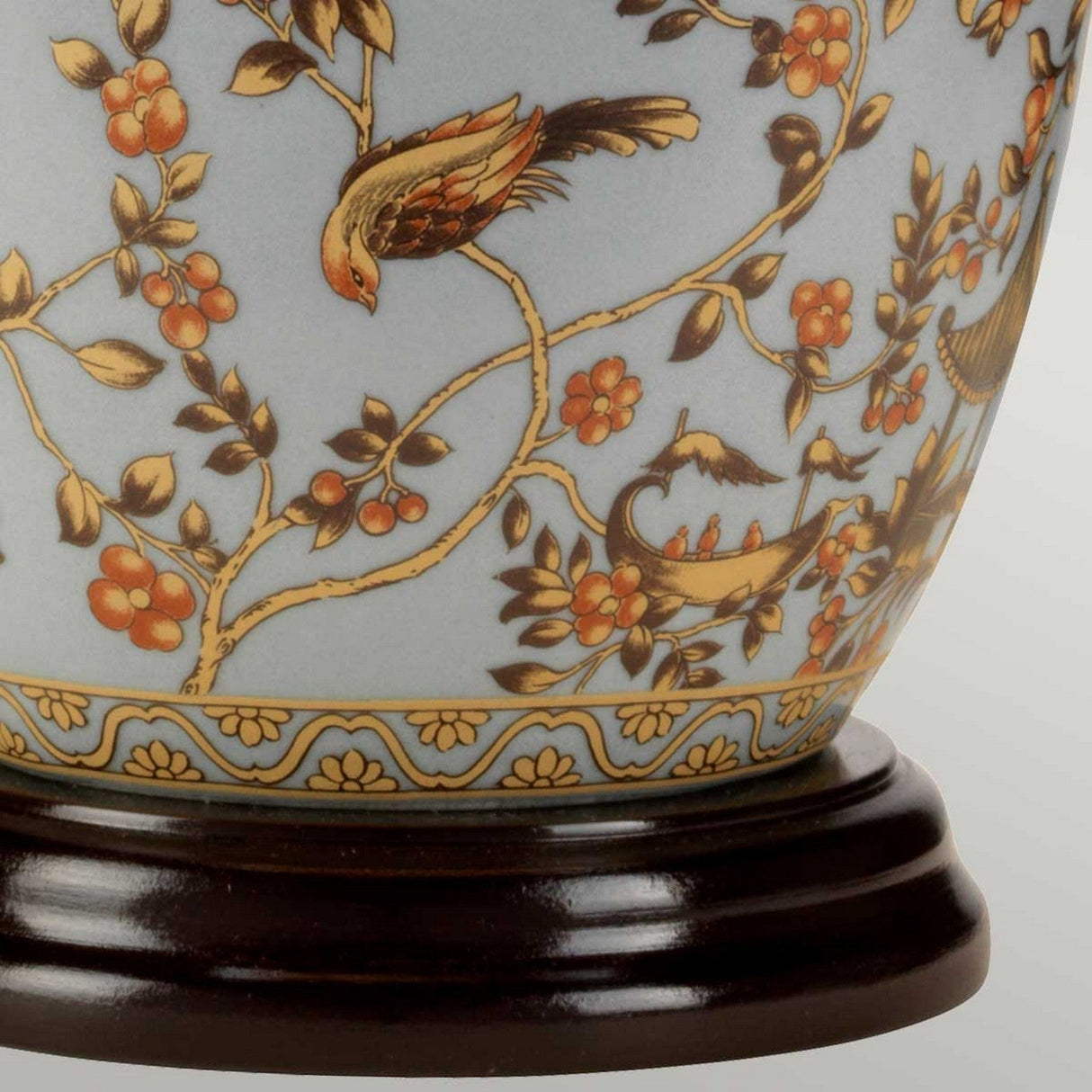 The Gold Birds 1 Light Table Lamp showcases a decorative design with a light blue glaze, featuring a bird perched on a branch amidst intricate floral patterns in gold and orange tones. It rests elegantly on a dark wooden Chinese porcelain base, exuding timeless elegance.