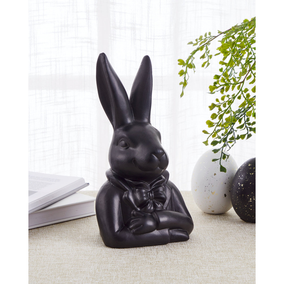 Gopeng Rabbit Ornament 23.2cm in Black, a sculpted figurine of a rabbit in a bow tie and jacket with folded arms, displayed on a table near a book and decorative eggs.
