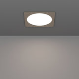 Gosmelle LED downlight recessed into a grey ceiling, showing a square satin nickel trim with a round white diffuser emitting warm light onto the surface below.