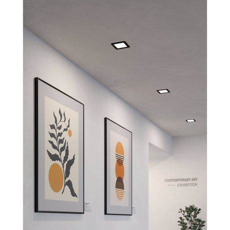 Square Gosmelle LED downlights with black steel trim recessed flush into a grey ceiling, lighting a hallway with framed artwork below.