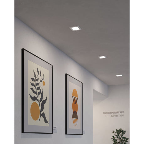 Gosmelle square LED downlight in white, 11.7 x 11.7cm, recessed into a grey ceiling in a gallery hallway lined with framed art prints.