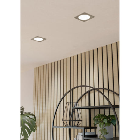 Gosmelle LED Downlight, 11.7 x 11.7cm square recessed fixtures with satin nickel bezels and round white diffusers, shown installed in a ceiling above a wood-slat wall and shelving unit.