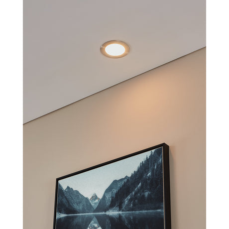 Gosmelle LED downlight recessed into a sloped white ceiling with satin nickel rim and warm white glow, installed near a wall with a framed landscape print.
