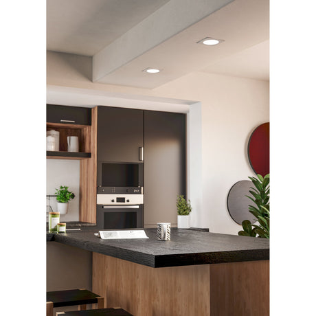 Gosmelle LED downlight, 11.9cm white square recessed fixture with round diffuser, shown installed flush in a kitchen ceiling beam above a dark countertop.