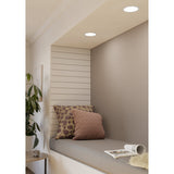 Gosmelle LED Downlight in white steel with a round flush diffuser, shown recessed in a ceiling above a window seat with cushions and a plant below.