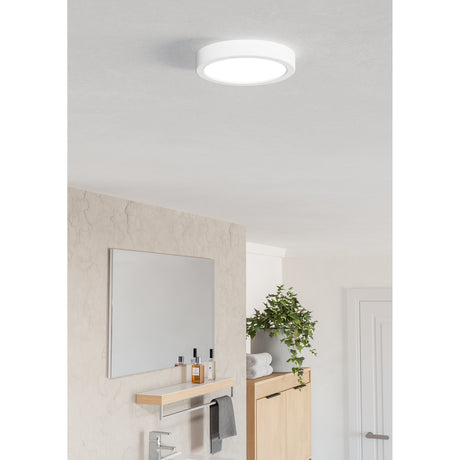 Gosmelle round LED downlight in white plastic, 16.6cm surface-mounted ceiling fixture with opal diffuser, shown illuminated on a bathroom ceiling near a mirror and wooden cabinet.