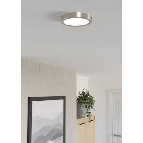 Gosmelle round LED downlight in satin nickel with white diffuser, flush-mounted on a ceiling above a hallway with a painting, plant, and wooden cabinet.