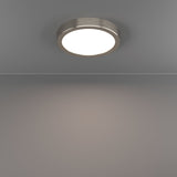 Gosmelle LED downlight in satin nickel, round low-profile ceiling fixture with white diffuser, shown illuminated on a grey ceiling and wall.