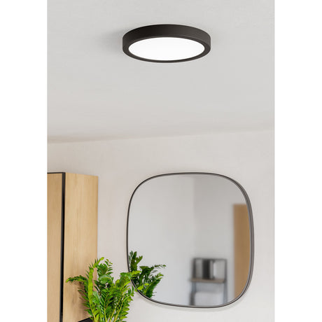 Gosmelle LED Downlight 21.1cm IP44 in black, round ceiling-mounted fixture with white diffuser, shown lit on a bathroom ceiling above a square wall mirror and wooden cabinetry.