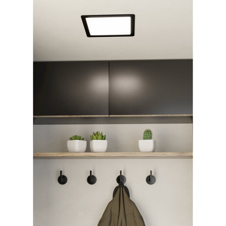 Gosmelle square LED downlight in black steel with white plastic shade, mounted on a ceiling above dark cabinets in a kitchen with an open shelf and wall hooks below.