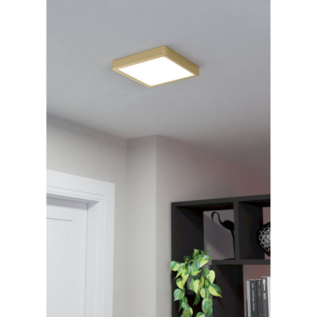 Gosmelle LED Downlight, 21 x 21cm square fixture with brushed brass frame and white diffuser, mounted flush on a ceiling above a hallway and shelving unit.