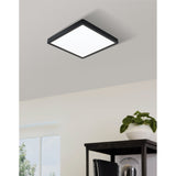 Gosmelle square LED downlight with black steel frame and white plastic diffuser, mounted flush on a light grey ceiling in a room with a plant and dark side table below.