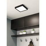 Gosmelle square LED downlight with black steel frame and white diffuser, mounted on a hallway ceiling above dark cabinetry and a shelf with plants.