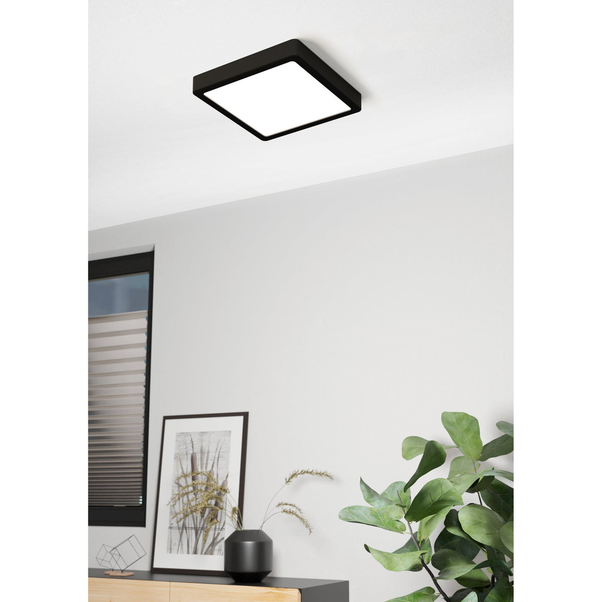 Gosmelle LED square downlight with black steel frame and white diffuser mounted on a ceiling, shown in a living room setting with a sideboard, framed artwork, and plant below.