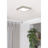 Gosmelle square LED downlight in satin nickel with a white diffuser, mounted flush on a white ceiling above a room with curtains and a shelf of plants.