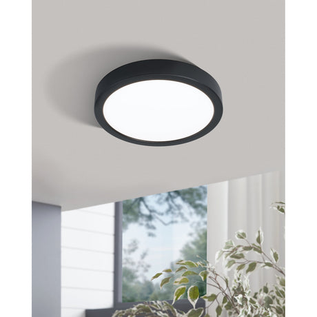 Gosmelle LED Downlight, a round 21cm ceiling fixture with black steel rim and white plastic diffuser, mounted flush on a light grey ceiling in a bright room setting.