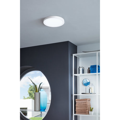 Gosmelle round LED downlight in white, 21cm flush ceiling fixture with opal diffuser, shown mounted on a grey bathroom ceiling near open shelving.